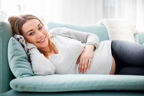 Femme enceinte relaxante et allongée sur le canapé à la maison regardant la caméra — Photo