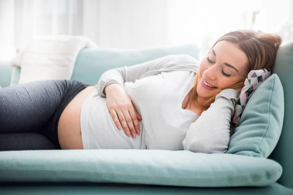 Mujer embarazada relajante y tumbada en el sofá en casa — Foto de Stock