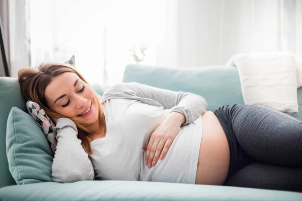 Беременная женщина отдыхает и лежит дома на диване — стоковое фото