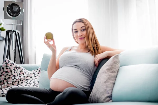 Nutrition et alimentation pendant la grossesse, Femme enceinte mangeant des fruits assis sur le canapé à la maison — Photo