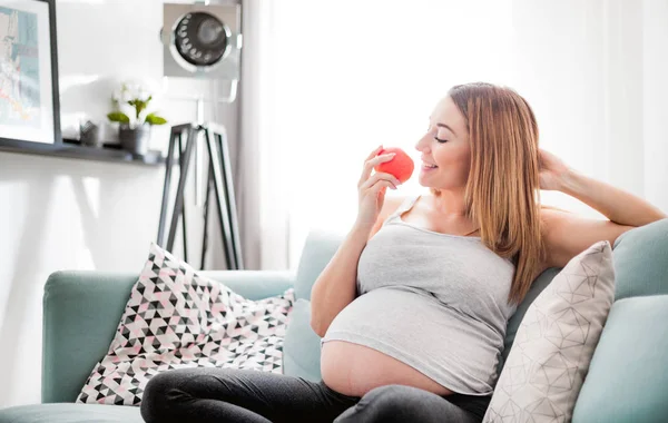 Питание и диета во время беременности, беременная женщина ест фрукты сидя на диване дома — стоковое фото