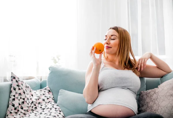 Nutrition et alimentation pendant la grossesse, Femme enceinte mangeant des fruits assis sur le canapé à la maison — Photo