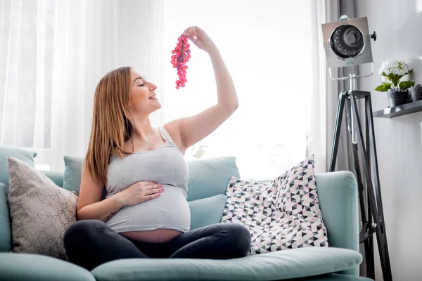 Nutrition and Diet during pregnancy, Pregnant woman eating fruits sitting on sofa at home