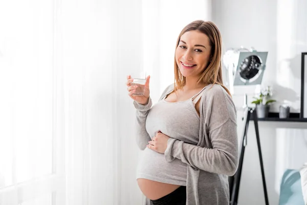 Zdraví během těhotenství, těhotná žena pije vodu na pohovce — Stock fotografie