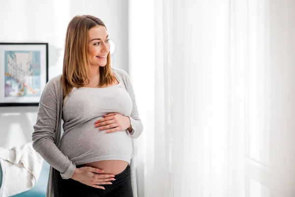 Gyönyörű terhes nő megérintette hasa állt az ablakon otthon — Stock Fotó