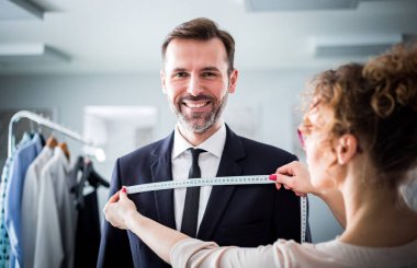 Atölyede dikiş elbisesi için gülümseyen istemciyi ölçmek için bant kullanan terzi