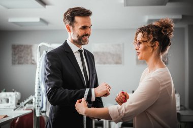 Atölyede dikiş elbisesi için gülümseyen istemciyi ölçmek için bant kullanan terzi