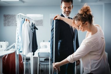 Atölyede dikiş elbisesi için istemciyi ölçmek için bant kullanan terzi