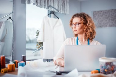Terzi dizüstü bilgisayar kullanarak, atölyede modern moda tasarımcısı