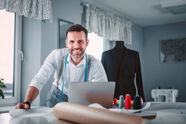 Çalışma sırasında dizüstü bilgisayar kullanarak çalışma masası üzerinde Terzi, atölyede modern moda tasarımcısı