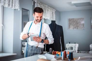 Çalışma sırasında dijital tablet kullanarak çalışma masası üzerinde terzi, atölyede modern moda tasarımcısı