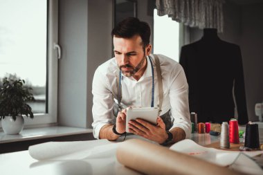 Çalışma sırasında dijital tablet kullanarak çalışma masası üzerinde terzi, atölyede modern moda tasarımcısı