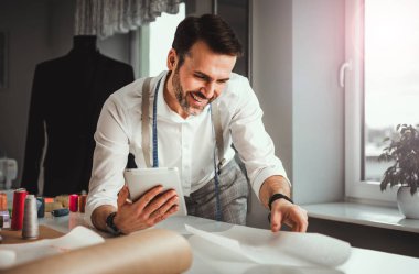 Çalışma sırasında dijital tablet kullanarak çalışma masası üzerinde terzi, atölyede modern moda tasarımcısı