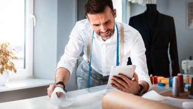 Çalışma sırasında dijital tablet kullanarak çalışma masası üzerinde terzi, atölyede modern moda tasarımcısı