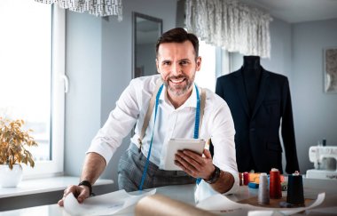 Çalışma sırasında dijital tablet kullanarak çalışma masası üzerinde terzi, atölyede modern moda tasarımcısı