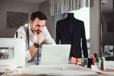 Atölyede dizüstü bilgisayar, modern moda tasarımcısı kullanarak iş sırasında Terzi