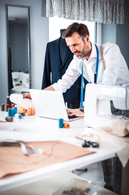 Atölyede dizüstü bilgisayar, modern moda tasarımcısı kullanarak iş sırasında Terzi