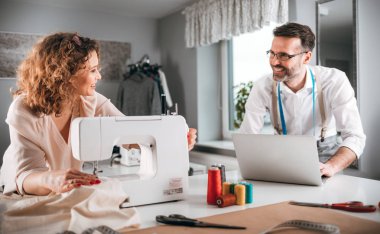 Moda tasarım stüdyosunda dizüstü bilgisayar ve dikiş makinesi kullanarak proje çalışmaları sırasında profesyonel terziler