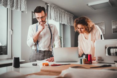 Moda tasarım stüdyosunda dizüstü bilgisayar ve dikiş makinesi kullanarak proje çalışmaları sırasında profesyonel terziler