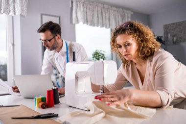 Moda tasarım stüdyosunda dizüstü bilgisayar ve dikiş makinesi kullanarak proje çalışmaları sırasında profesyonel terziler