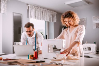 Moda tasarım stüdyosunda dizüstü bilgisayar ve dikiş makinesi kullanarak proje çalışmaları sırasında profesyonel terziler