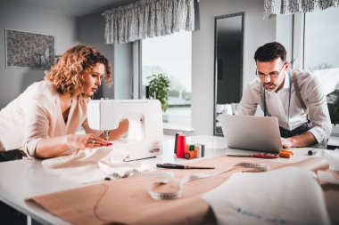 Moda tasarım stüdyosunda dizüstü bilgisayar ve dikiş makinesi kullanarak proje çalışmaları sırasında profesyonel terziler