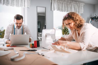 Moda tasarım stüdyosunda dizüstü bilgisayar ve dikiş makinesi kullanarak proje çalışmaları sırasında profesyonel terziler