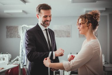 Moda tasarım stüdyosunda dikiş takım elbise için müşteri ölçmek için bant kullanarak profesyonel terzi