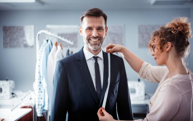 Moda tasarım stüdyosunda dikiş takım elbise için müşteri ölçmek için bant kullanarak profesyonel terzi