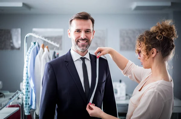 Schneiderin misst lächelnden Kunden mit Klebeband für Nähanzug im Atelier — Stockfoto