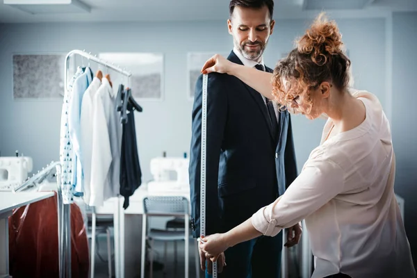 Atölyede dikiş elbisesi için istemciyi ölçmek için bant kullanan terzi