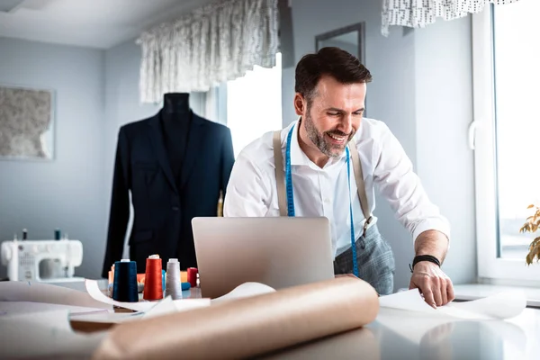 Tailor over work desk using laptop during work, modern fashion designer at workshop