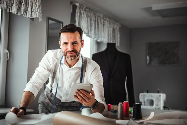 Tailor over work desk using digital tablet during work, modern fashion designer at workshop