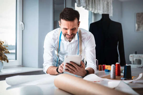 Tailor over work desk using digital tablet during work, modern fashion designer at workshop