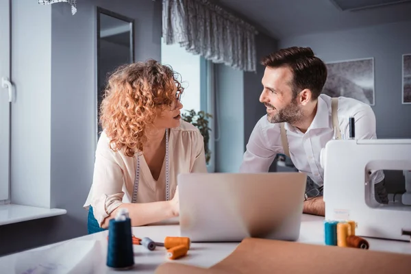 Alfaiates profissionais durante o trabalho no projeto usando laptop no estúdio de design de moda — Fotografia de Stock