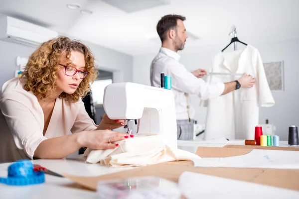 Professional tailors during work on project in fashion design studio, using sewing equipment