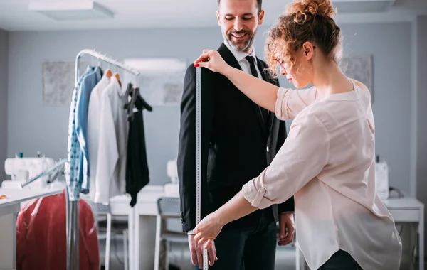 Moda tasarım stüdyosunda dikiş takım elbise için müşteri ölçmek için bant kullanarak profesyonel terzi