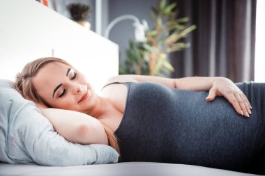 Yatakta oturan ve karnına dokunmadan genç hamile kadın, çocuk beklenti kavramı