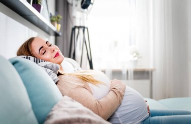 Hamile genç kadın kanepede oturan ve evde rahatlatıcı