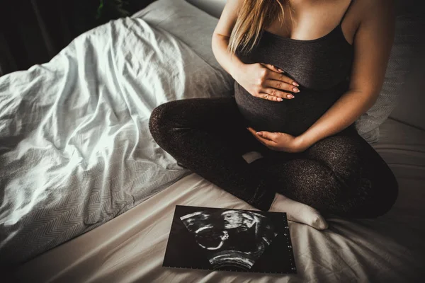 孕妇坐在床上 看着她的婴儿超声波照片 — 图库照片