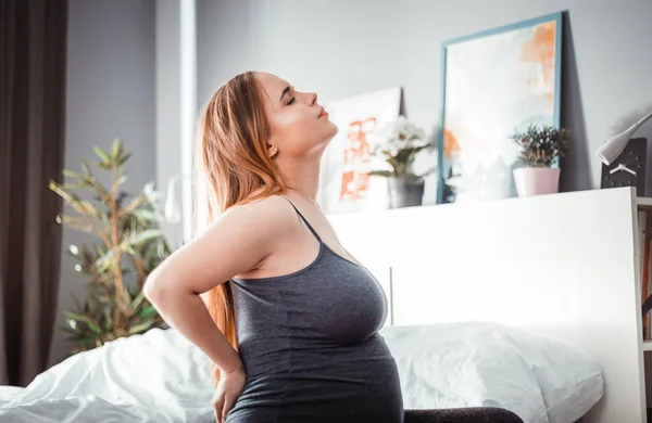 Lower back pain during pregnancy, pregnant woman sitting on bed at home