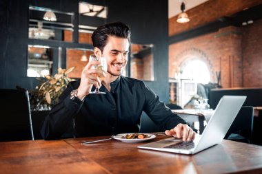 Genç yakışıklı işadamı restoranda yemek yiyor ve laptop kullanıyor.