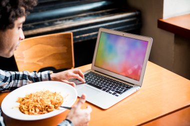 Restoranda masada dizüstü boş boş ekran, yemek yaparken bilgisayar kullanarak genç adam