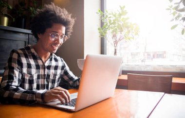 Restoranda otururken dizüstü bilgisayar kullanarak gözlük Afrikalı adam, Genç insanlar kavramı çalışma