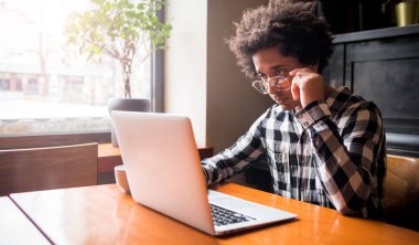 Restoranda otururken dizüstü bilgisayar kullanarak gözlük Afrikalı adam, Genç insanlar kavramı çalışma