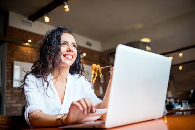 Restoranda dizüstü bilgisayar üzerinde çalışan Latin Genç kadın, iş sırasında mola yeme