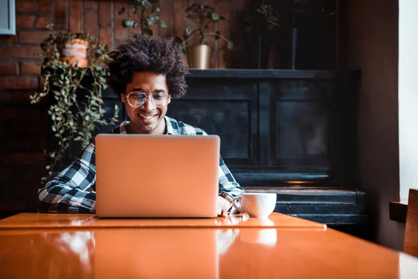 African man in glasses using laptop while sitting at restaurant, concept of young people working — Stock Photo, Image