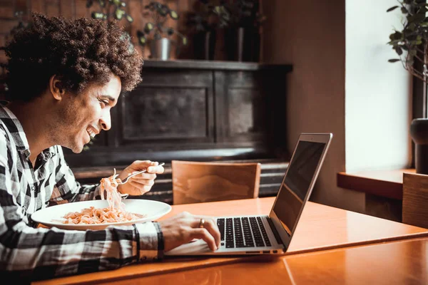 Joven afroamericano comiendo y trabajando en laptop en restaurante — Foto de Stock