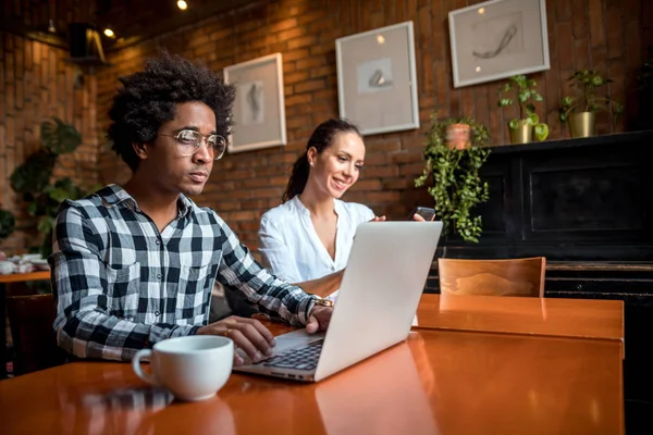 Reunión del equipo de negocios multiétnicos en la cafetería, trabajando con computadora portátil y teléfono inteligente — Foto de Stock