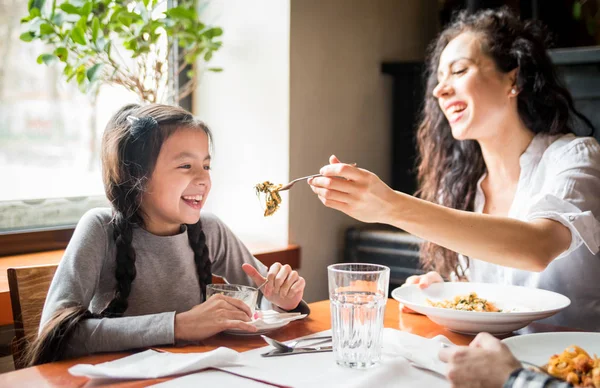Latin mom and daughter eating together lunch at restaurant, multiethnic family having fun